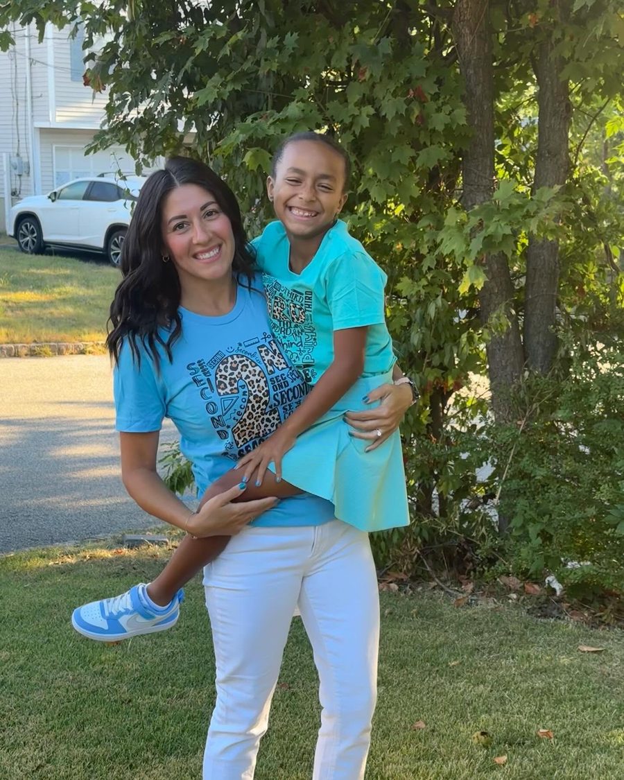 Deej smiling outdoors while holding Imani, both wearing custom shirts